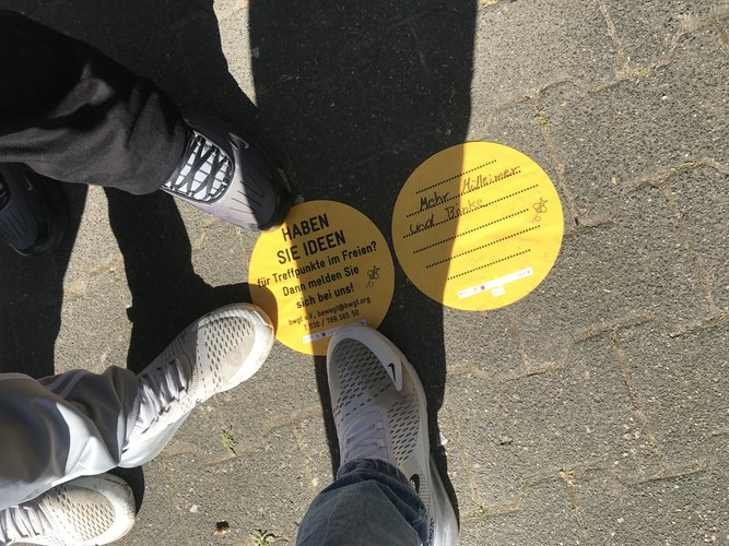 Füße und ein Auflkleber am Boden, auf dem steht:Haben Sie Ideen für Treffpunkte?