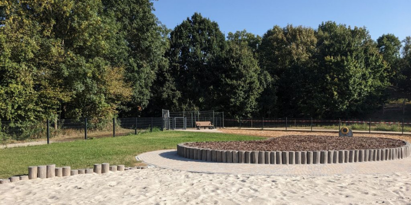 Eingezäunte Fläche mit Sand, im Hintergrund Bäume