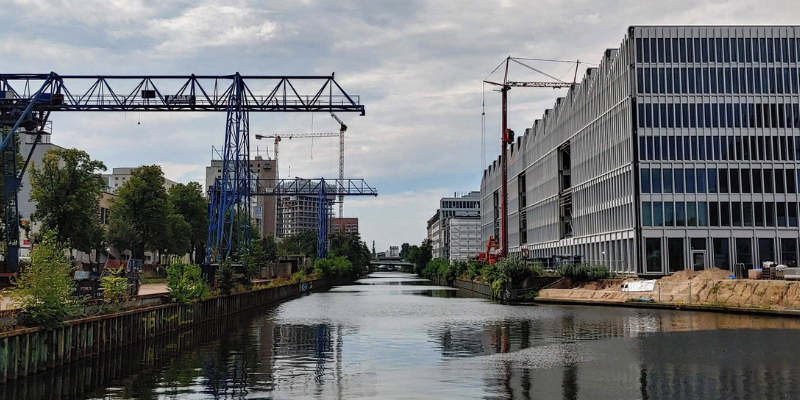 Blick auf Schifffahrtskanal mit Baukränen und modernen Gebäuden an dem Ufer