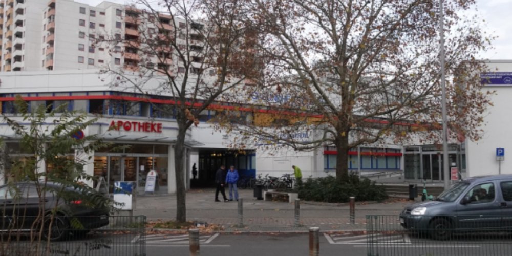 Flaches Gebäude vor einem Hochhaus mit Apotheke
