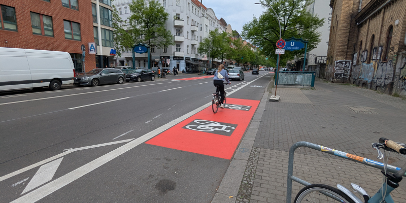 Eine Fahrradfahrerin fährt auf einem rot markierten Radweg an einer Straße