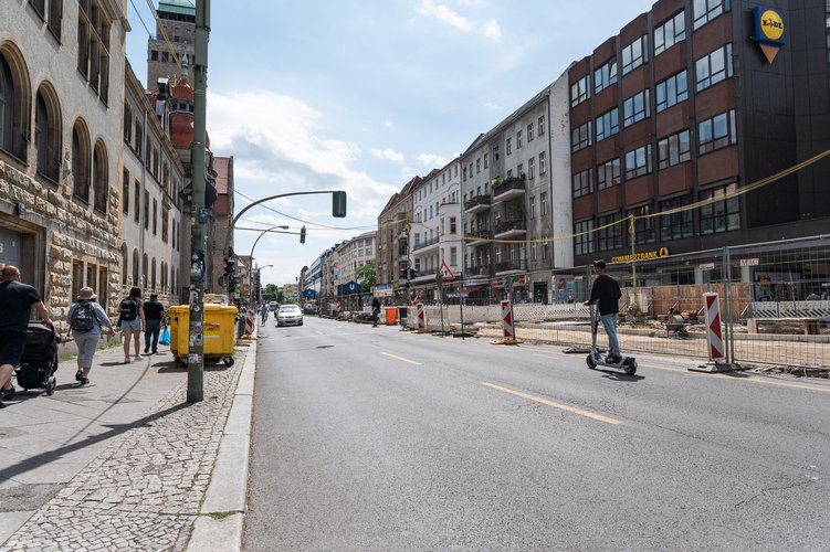Befahrende Straße mit Häuserfronten auf beiden Seiten.