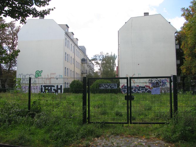 Eine eingezäunte Wiese, im Hintergrund sind Häuser zu sehen.