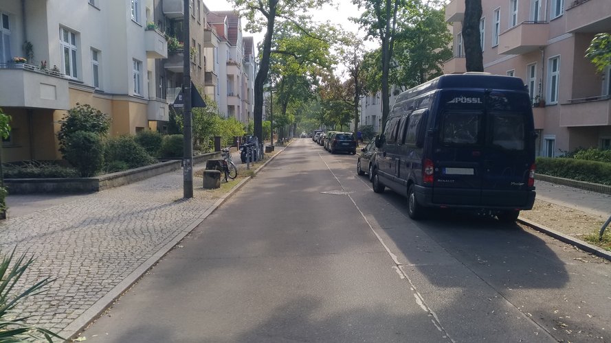 Hentigstr.: Wohnstraße mit zwei Baumreihen und einseitig geparkten Autos.