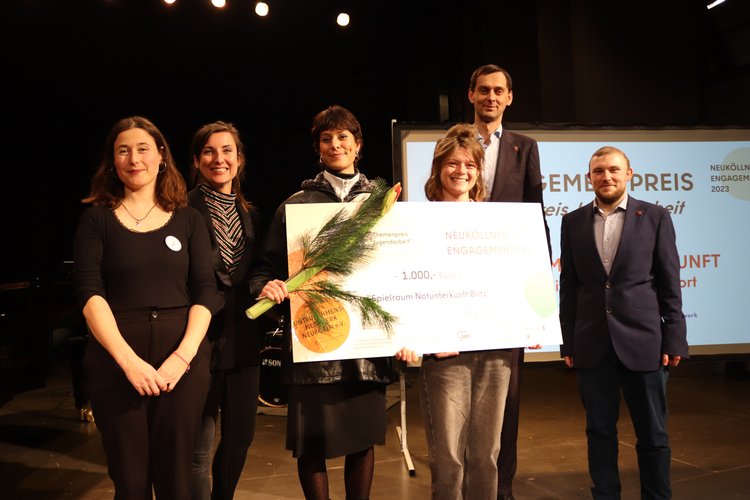 Ehrung eines Projektes auf der Bühne. Personen haben großen Scheck in der Hand