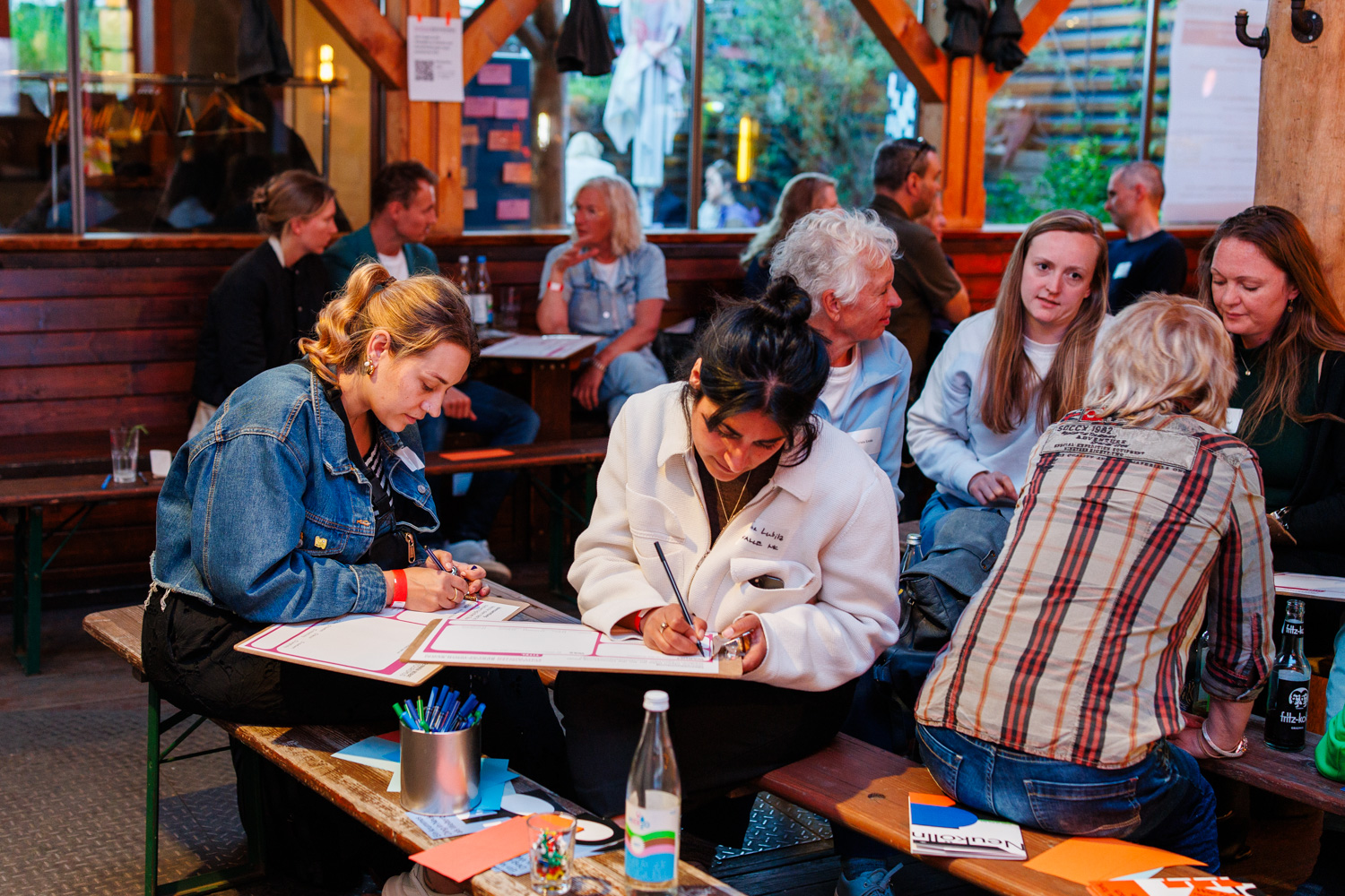 Einblick in die Workshopphase: In mehreren Kleingruppen werden die Ideensteckbriefe für Projekte und Maßnahmen für eine stadtverträglich Tourismusentwicklung ausgefüllt. Zu sehen sind mehrere Menschen, die sich austauschen und ihre Ideen auf Klemmbrettern festhalten.