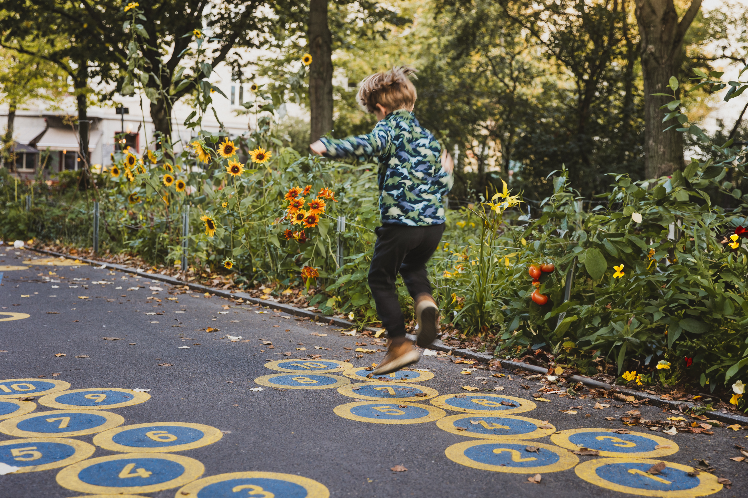Lausitzer Platz: Ein Kind spielt Hüpfekästchen vor einem Blumen- und Gemüsebeet.