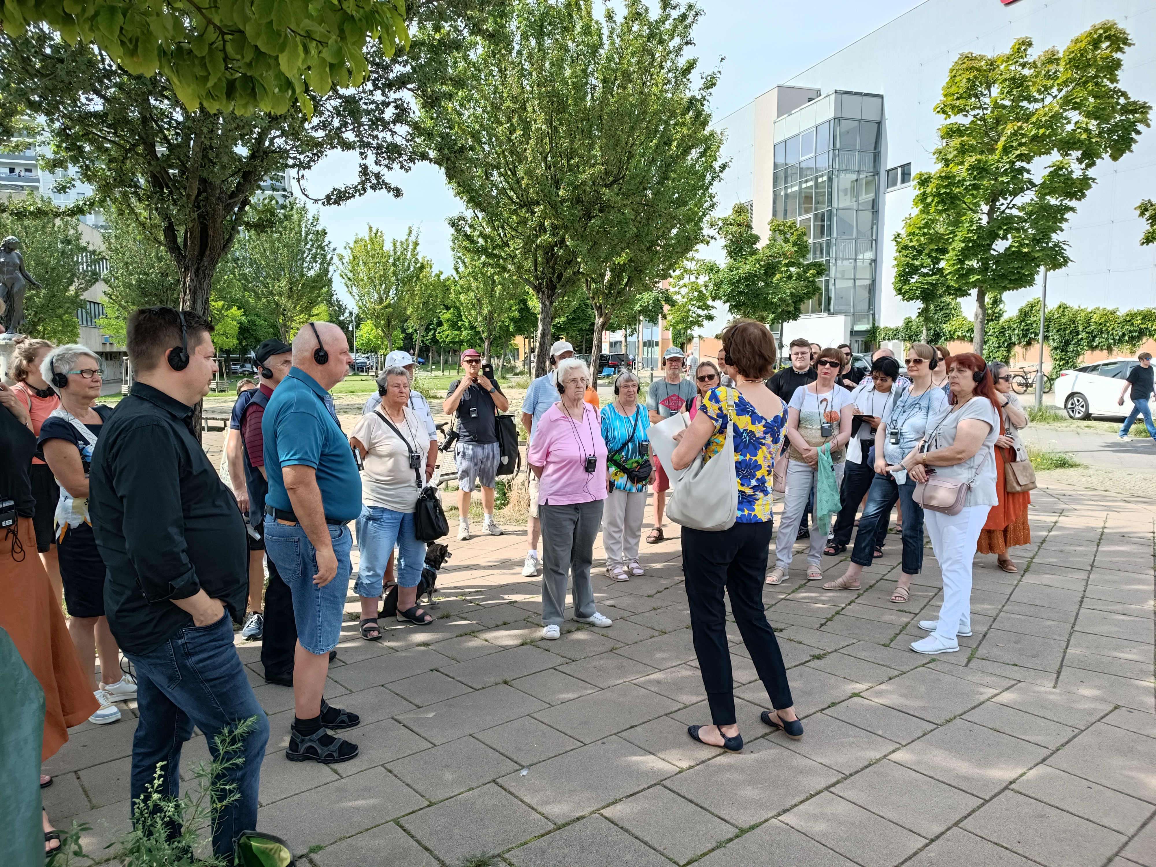 Gruppe von Personen auf einem Platz mit Kopfhörern, die den Sprechern des Rundgangs zuhören